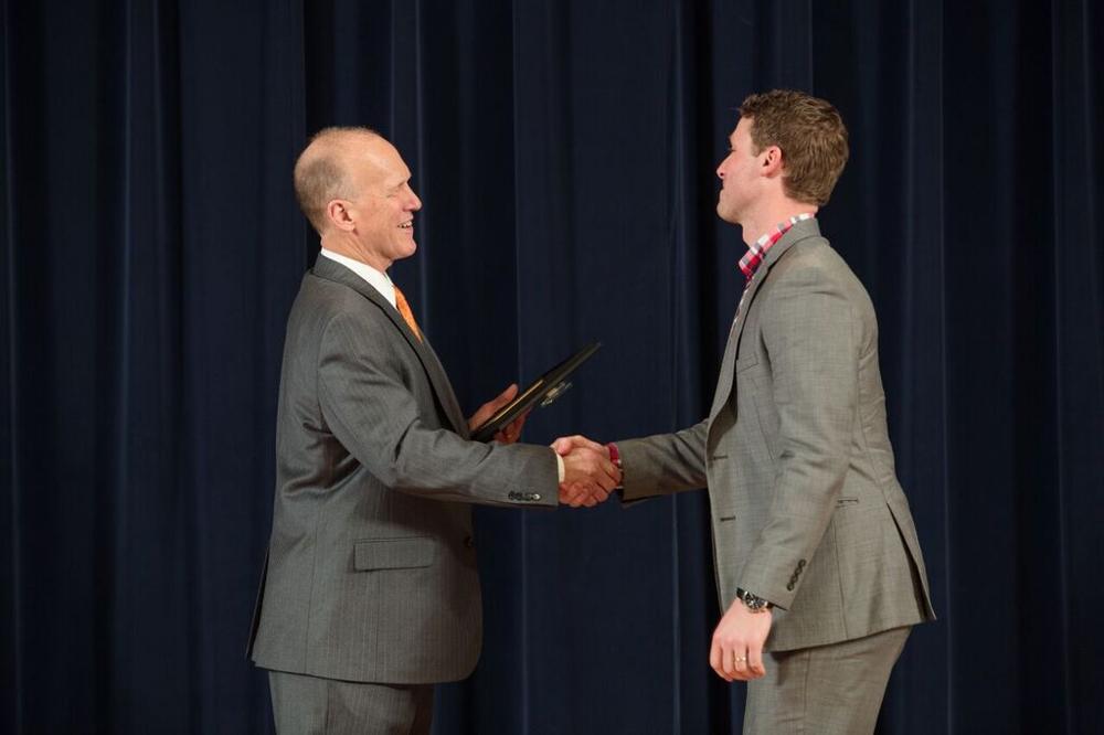 Doctor Potteiger shaking hands with an award recipient in a light grey suit and a red plaid shirt